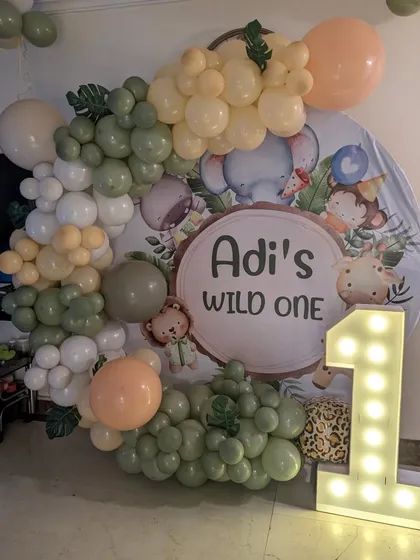 Celebrating a 'Wild One' first birthday with a trendy jungle-themed backdrop. This setup uses a gentle, earthy color palette of sage green and beige balloons, a personalized sign, and a large marquee number to mark the special milestone.