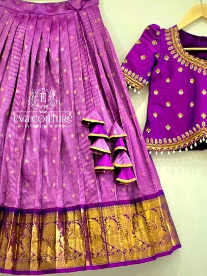 This set includes a purple pleated skirt with a gold border and a matching blouse with delicate butti work and pearl detailing.