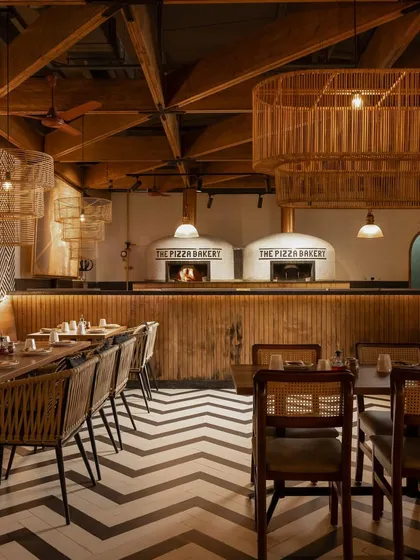The interior of 'The Pizza Bakery' in Whitefield features a rustic, vintage vibe with wooden rafters, hand-plastered walls, and prominent pizza ovens.