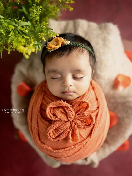 A close-up of a newborn wrapped in a warm orange swaddle, looking like a precious gift. The soft textures and colors create a cozy and inviting portrait.