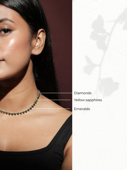 The Leafline Necklace worn by a model, showcasing its delicate sparkle and how it sits beautifully on the collarbone. The gems are labeled to highlight the combination of diamonds, yellow sapphires, and emeralds.
