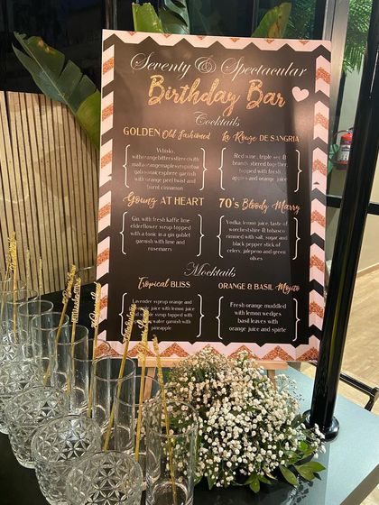 A spectacular birthday bar menu for a 70th celebration. The custom-designed menu board is adorned with a baby's breath arrangement, tying it into the overall event decor.