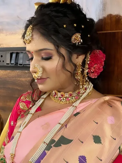 A close-up profile shot, focusing on the intricate hairstyle with floral and gold accessories and the flawless makeup.
