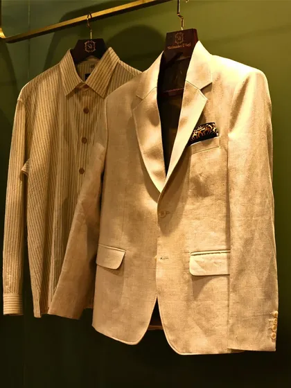 A beige blazer and striped shirt hanging together, ready for a client. This image captures a moment in our studio and shows a classic, ready-to-wear combination.