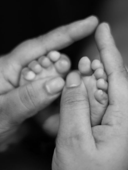 A detailed black and white macro shot of a parent's hands gently cradling their newborn's tiny feet.