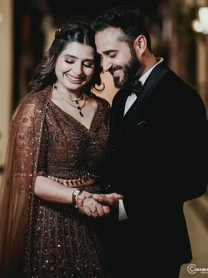 A candid moment of shared laughter between the couple during their engagement shoot. The groom is dressed in a classic tuxedo, while the bride wears a stunning sequined lehenga.
