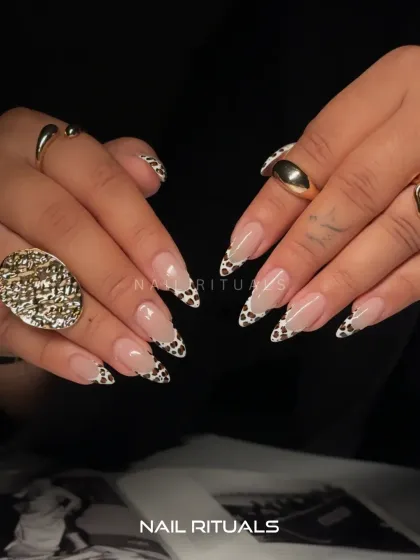 A modern twist on a classic. These almond-shaped nail extensions feature a chic cow print design on the French tips, giving a playful yet sophisticated finish to a nude manicure.
