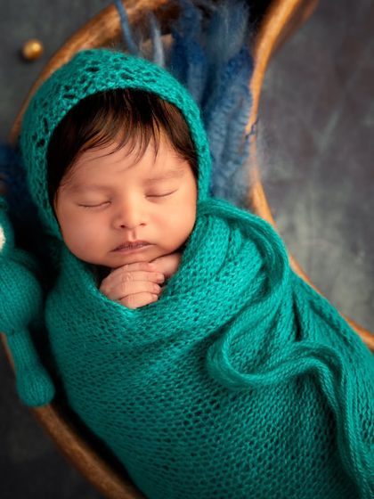 A celestial dream in shades of teal and blue. This close-up shows the baby with a matching knitted bonnet and a tiny bear companion, ready for a journey to the stars.