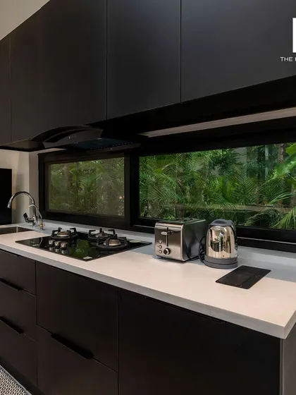 A sleek, modern kitchen with all-black cabinetry and a white countertop. The window above the sink provides natural light and a view of the garden, making the space feel connected to the outdoors.