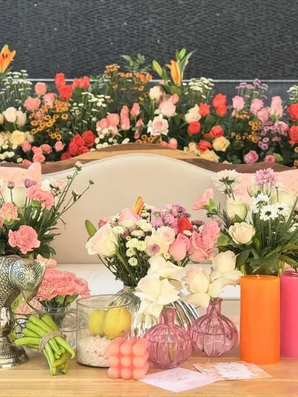 The main seating arrangement for the couple, set against a backdrop of vibrant orange and pink flowers. The table is adorned with colorful vases and unique decor items.