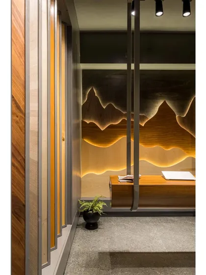 The entrance to the showroom, where a curved wooden wall guides visitors inside. The view is framed to immediately draw attention to the back-lit, mountain-inspired veneer art piece.