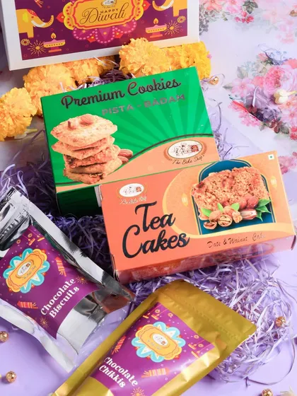 The 'Prosperity Box' is a curated Diwali hamper containing Pista Badam Cookies, a Date & Walnut Tea Cake, and packs of our Chocolate Chikkis and Chocolate Biscuits. It's a perfect mix of traditional and modern flavors.