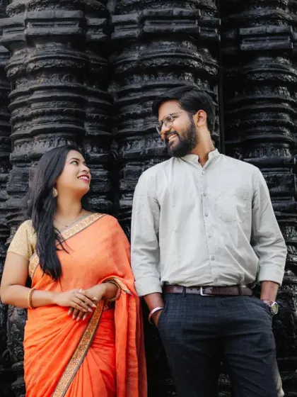 Using dramatic backdrops to create powerful images. Here, the couple shares a look in front of a heavily carved, dark stone wall, which contrasts beautifully with the bride's bright orange saree.