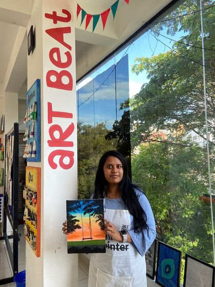 A participant with her finished sunset painting. The beautiful colors and serene scene make it a piece she can be proud of.