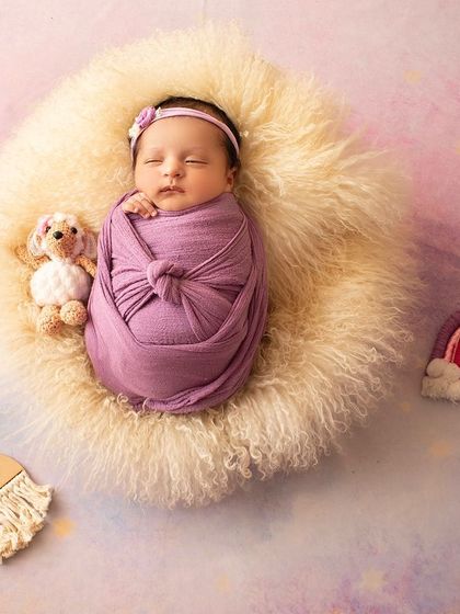 A one-month-old baby sleeps peacefully in a fluffy basket, surrounded by a rainbow and a starry backdrop.