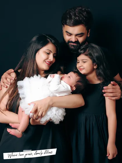 Welcoming a new baby is a milestone for the whole family. This portrait shows a family of four, with the parents and older sister all focused on the newest member, creating a sense of unity and love against a classic dark backdrop.