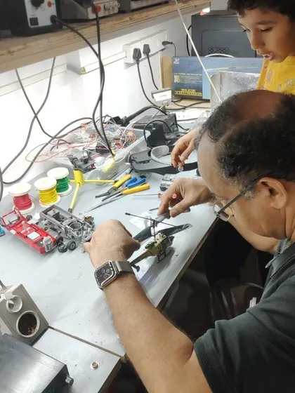 A mentor and a young boy work together to repair a toy helicopter at a makerspace. This image captures the joy of collaborative problem solving and the satisfaction of bringing a favorite toy back to life.