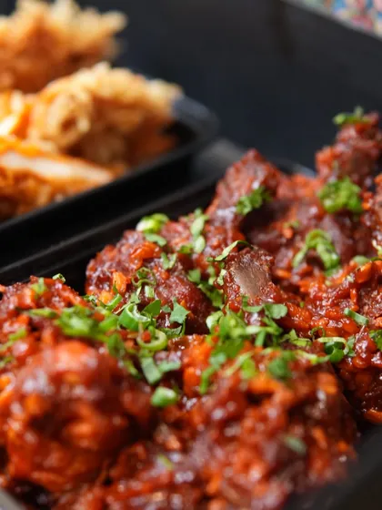 A close-up of our Chicken Lollipop, generously coated in a rich, dark sauce and garnished with fresh spring onions.