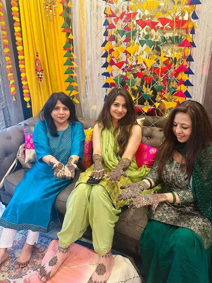 A lovely group photo showing three generations or friends enjoying the mehndi tradition together, each with their own unique design.