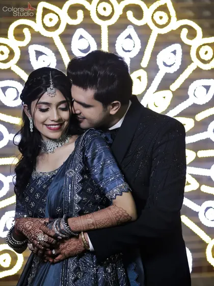 A sweet moment with the groom whispering to his bride, set against a beautifully lit peacock-feather-themed backdrop.