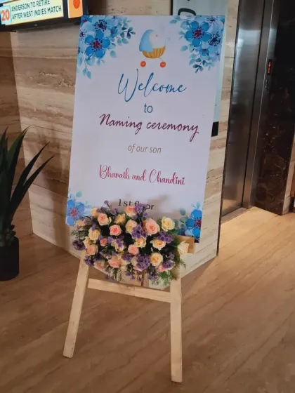 A simple and elegant welcome easel for a naming ceremony, with a custom watercolor-style sign and a fresh flower arrangement.