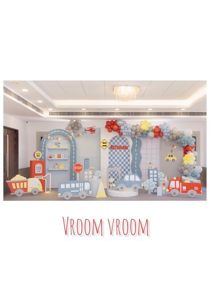 A full-stage view of our 'Vroom Vroom' transportation party. The setup includes a fire truck, bus, and car props, along with a road-themed backdrop and a colorful balloon arch.