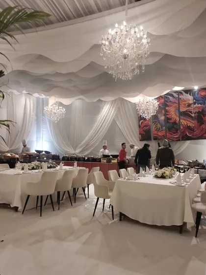 An all-white dining area for a reception, featuring a unique wavy ceiling drape, crystal chandeliers, and a live-cooking buffet station, creating a clean and luxurious dining experience.