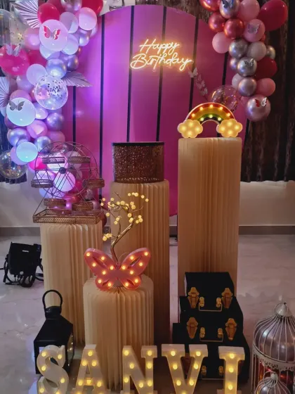 A vibrant butterfly-themed birthday decoration with a pink arched backdrop, marquee letters, and a variety of props like a mini ferris wheel and lanterns.