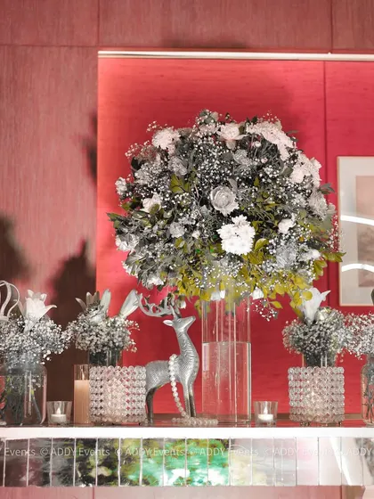 A royal welcome setup featuring a mirrored console table adorned with silver and white floral arrangements, candles, and a decorative silver deer.