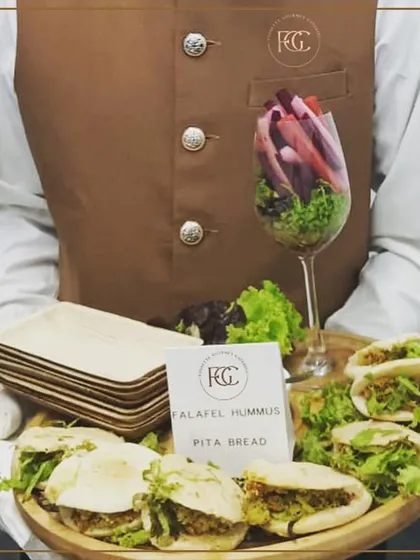 Our take on a Mediterranean classic. A server holds a tray of mini Falafel Hummus Pita Pockets, accompanied by a glass of fresh vegetable crudités for a healthy and delicious option.