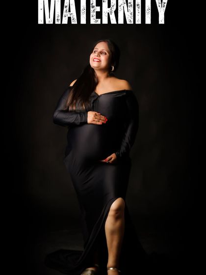 A powerful and confident portrait of a woman in a black gown against a black background. The dramatic lighting highlights her form, celebrating the strength and beauty of pregnancy.