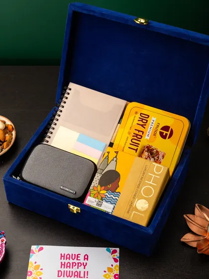 For the tech-savvy professional, this hamper in a royal blue velvet box is a perfect fit. It combines a portable speaker and a notebook with sticky notes, along with Phool incense cones and dry fruit bites for a balanced gift of work and relaxation.