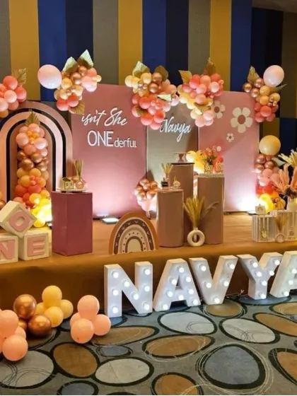 A trendy and warm boho-chic theme for a "ONEderful" first birthday. This decor features earthy tones of rose gold and terracotta, with light-up letters spelling the name "NAVYA" for a personalized focal point.