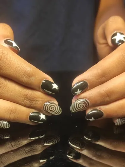 A bold black and white graphic design with stars and hypnotic swirls on short, rounded nails.