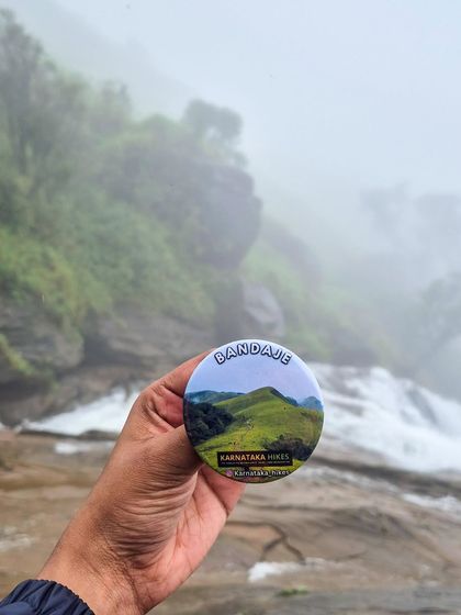 A close-up of our Bandaje badge, held against the misty backdrop of the falls.
