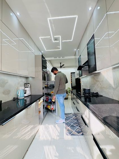 Inspecting the pantry unit and drawers in this newly installed parallel kitchen. The design features glossy grey cabinets, a black granite countertop, and modern profile lighting on the ceiling.