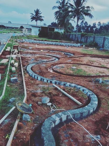 A winding stone curb takes shape on site, defining the edge between a future pathway and a planting area. This image captures the hands-on craftsmanship required to execute a landscape design.