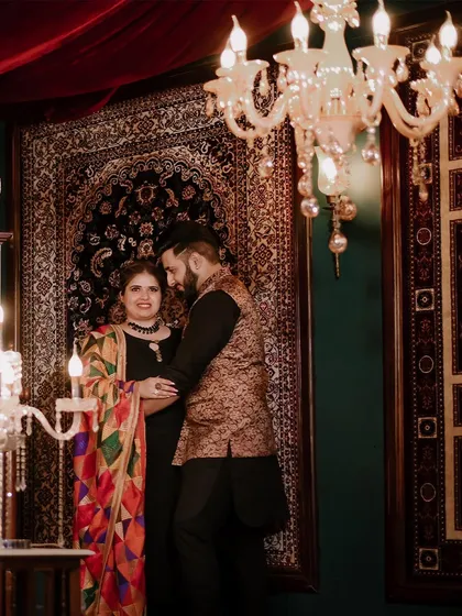 A rich and warm portrait from an indoor pre-wedding shoot. The traditional outfits, ornate carpet, and chandelier create a luxurious and classic Punjabi vibe.