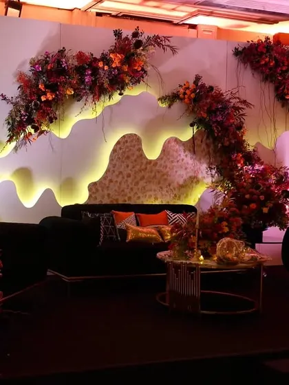 A wider shot of the stage and lounge area, demonstrating how the backlit backdrop, floral decor, and comfortable seating come together to create an inviting space for guests to relax.