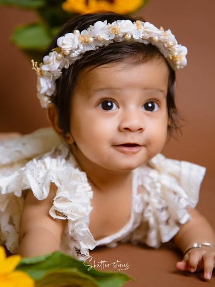 A beautiful close-up of a baby girl during her sitter session, surrounded by sunflowers and wearing a delicate floral headband.