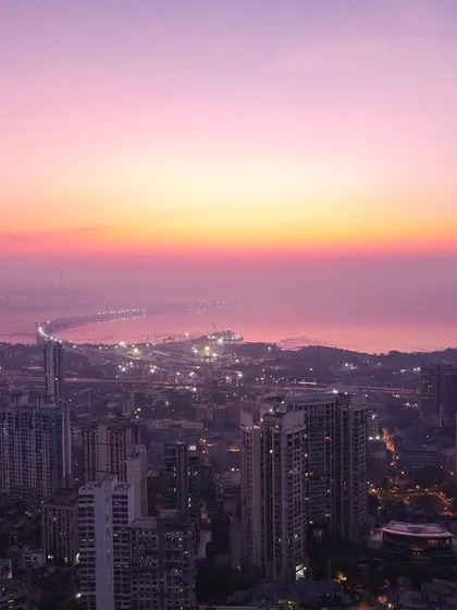 An early morning drone shot over Mumbai, showing the Bandra-Worli Sea Link and the city skyline bathed in the soft, hazy light of sunrise.