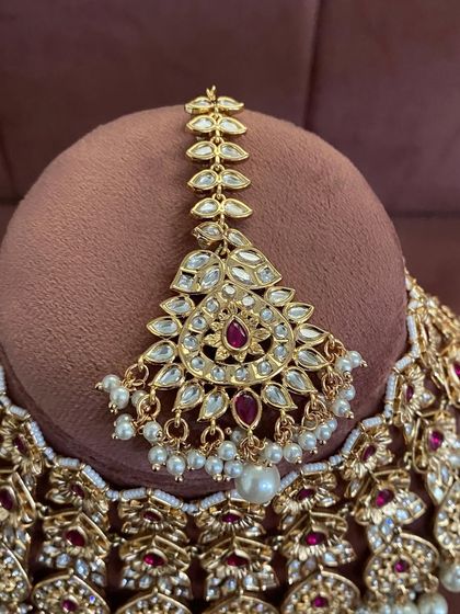 A detailed shot of a maang tikka from a red and pearl kundan set, showing the quality of the stones.