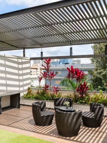 This angle highlights the built-in ledge and storage unit on the terrace, designed to function as an outdoor pantry or mini-bar. The slatted design of the unit mirrors the pergola above, creating a cohesive and functional design language.
