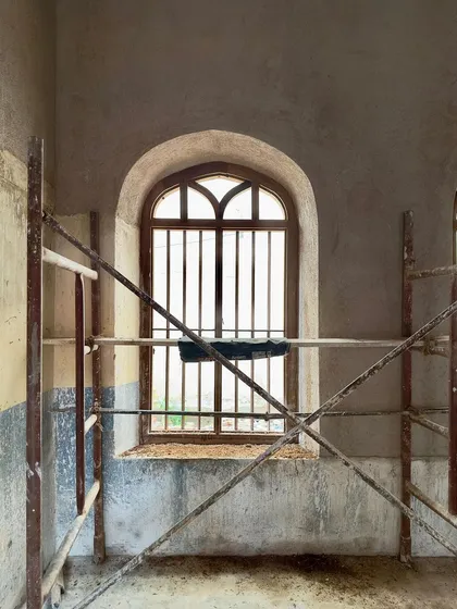 A newly restored arched window, still surrounded by scaffolding. The clean lines of the new plaster and the repaired window frame contrast with the raw state of the surrounding walls, showing the project in transition.