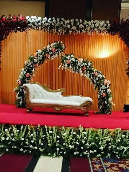 This is a classic wedding reception stage I designed at the Eros Hotel. The setup features a grand floral arch in red and white, a smaller broken arch for a modern touch, and a clean white diwan, creating a rich and elegant look.
