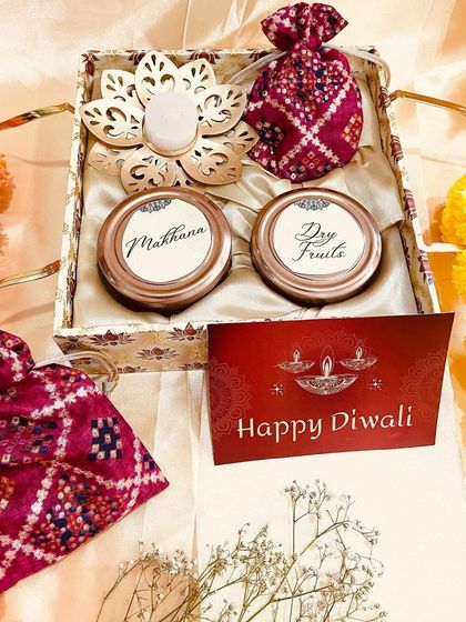 A classic Diwali gift set featuring two jars for makhana and dry fruits in a patterned box, accompanied by a diya and traditional potlis.