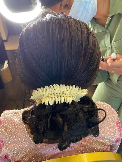 A close-up of a sleek and elegant bridal bun, adorned with a simple jasmine gajra. This is a classic and sophisticated choice for a reception or formal event.