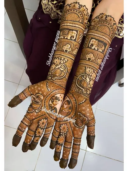 A full view of a custom bridal design. The palms feature couple portraits, while the arms are decorated with bands of peacocks and elephants, creating a rich and symbolic look.