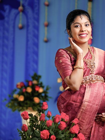 A joyful portrait of the expecting mother at her baby shower. Her bright smile and traditional attire are perfectly complemented by the colorful floral arrangements and peacock-themed backdrop.
