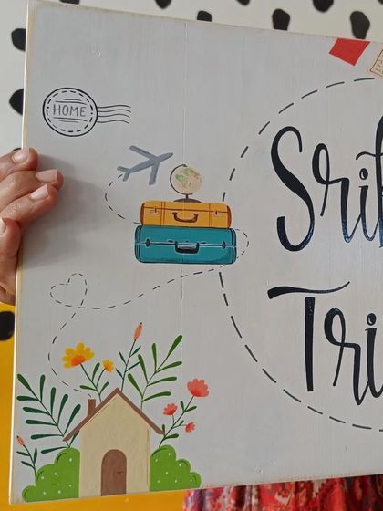 A detail shot of the "Srikant and Trisha" name board, focusing on the travel-themed illustrations that tell the story of their life together.